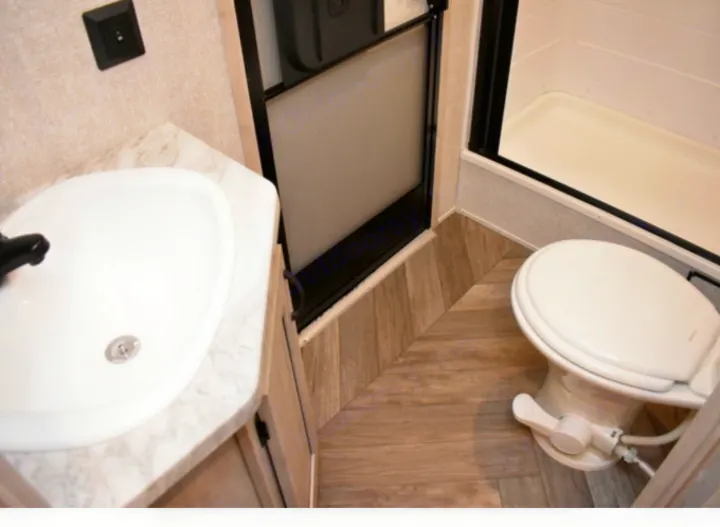 Inside a functional RV rental bathroom: a convenient sink, toilet, and shower stall with stylish wood-look flooring.. East to West Other 2022