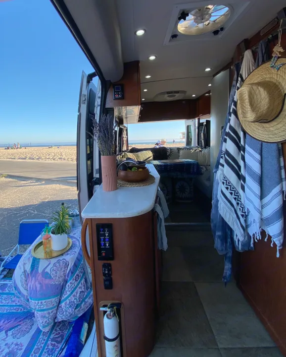 RV rental at the beach: A cozy camper van interior with kitchen & bed, opening to a vibrant sandy beach & ocean.. Pleasure-Way Pleasure-Way Class B 2016