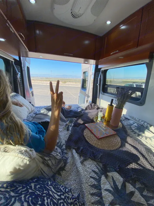 Relaxing inside an RV rental with open doors, showing a peace sign, comfy bed, and a scenic outdoor view.. Pleasure-Way Pleasure-Way Class B 2016