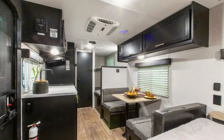 Modern RV rental interior with compact kitchen, dining area, bunk beds, and part of a sleeping space. Ideal for travel.. Forest River Cherokee Wolf Pup 2022