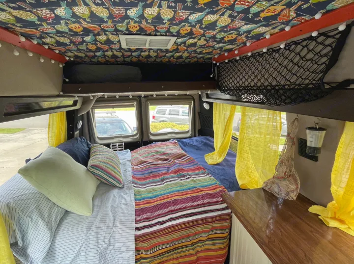 Cozy camper van interior for rv rental, featuring a comfortable bed, vibrant blankets, and unique ceiling art.. Ford Econoline 2006