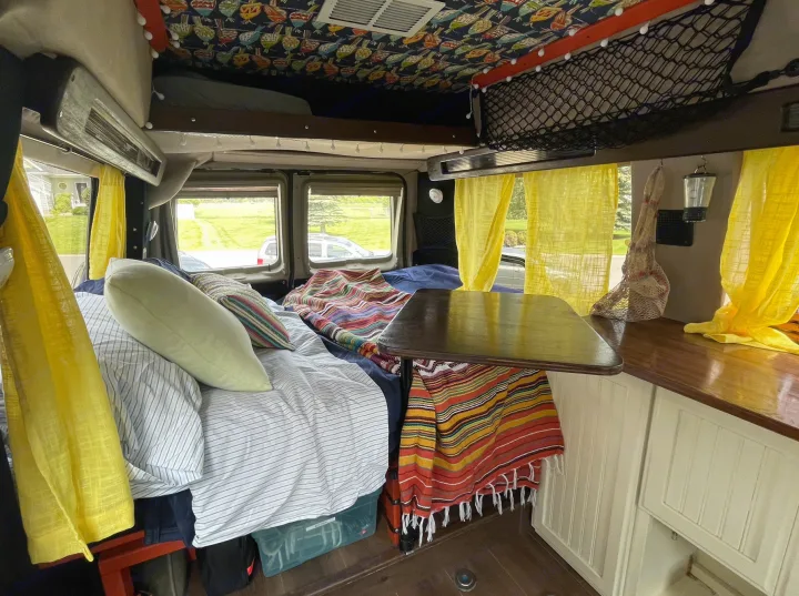 Cozy RV rental camper van interior with bed, kitchen counter, and bright yellow curtains for travel.. Ford Econoline 2006