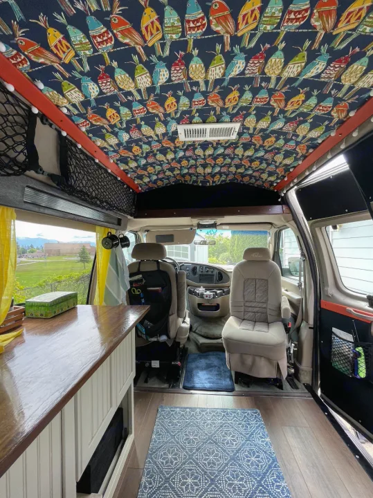Unique RV rental interior with colorful bird-patterned ceiling, functional counter, and spacious driver's area for comfortable travel.. Ford Econoline 2006