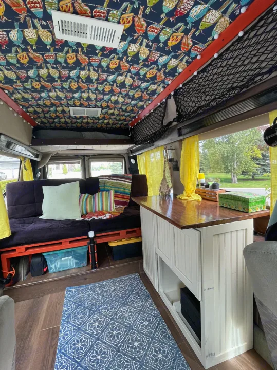 RV rental: Inside a cozy camper van featuring a vibrant bird-patterned ceiling, comfy futon, wood counter, and storage.. Ford Econoline 2006