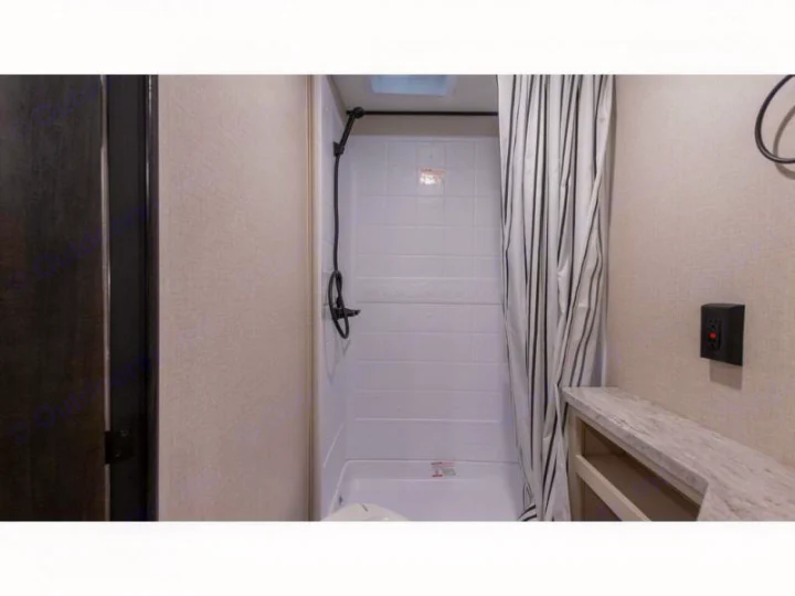 Explore this RV rental's compact bathroom featuring a shower with striped curtain, small vanity, and wall panel.. Autumn Ridge 26BHS 2022