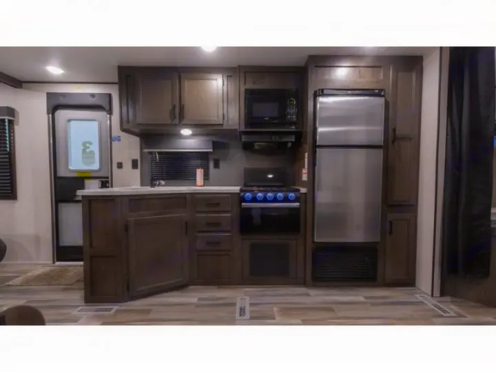 RV rental interior: modern kitchen with stainless steel refrigerator, microwave, stove, dark wood cabinets, and wood-look floor.. Autumn Ridge 26BHS 2022