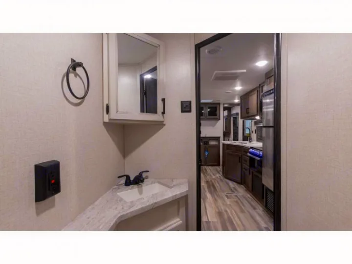 RV rental interior: A compact bathroom vanity with sink and mirror is on the left, leading to a functional kitchen on the right.. Autumn Ridge 26BHS 2022