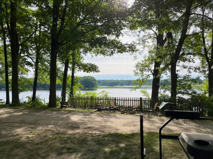 RV rental offers serene lakeside escape: a shaded outdoor area with trees, a fence, swing, and fire pit by the water.. Autumn Ridge 26BHS 2022