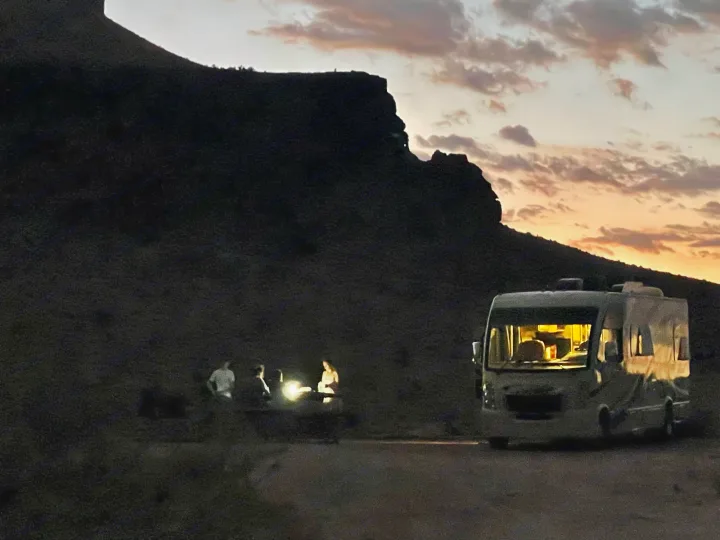 **RV rental** illuminated at dusk, with people gathered outdoors near mountains under a sunset sky.. Thor Vegas 2017