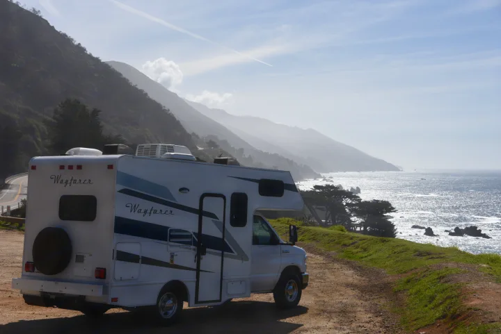 Scenic rv rental adventure! A white Wayfarer RV parked by a stunning coastline with mountains and a sparkling ocean.. Wayfarer 19 TM 2020