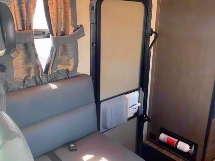 Inside an RV rental: a gray bench seat next to the main entry door with a storage cubby and a fire extinguisher.. Wayfarer 19 TM 2020