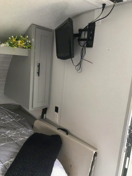 RV rental bedroom featuring a wall-mounted TV, overhead storage cabinet, and bed. Ideal for comfortable travel.. Forest River Wildwood 2021