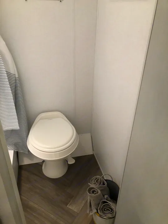 RV rental bathroom: compact toilet, striped shower curtain, & rolled towels, perfect for your travels.. Forest River Wildwood 2021