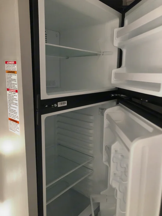 An open, empty refrigerator in an RV rental, revealing clean shelves and door storage. Ready for your trip!. Forest River Wildwood 2021