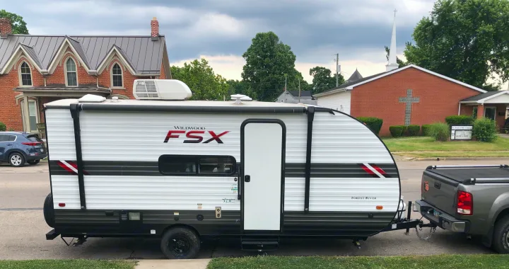 Wildwood FSX travel trailer, a great RV rental option, is shown hitched to a pickup truck by a church.. Forest River Wildwood 2021