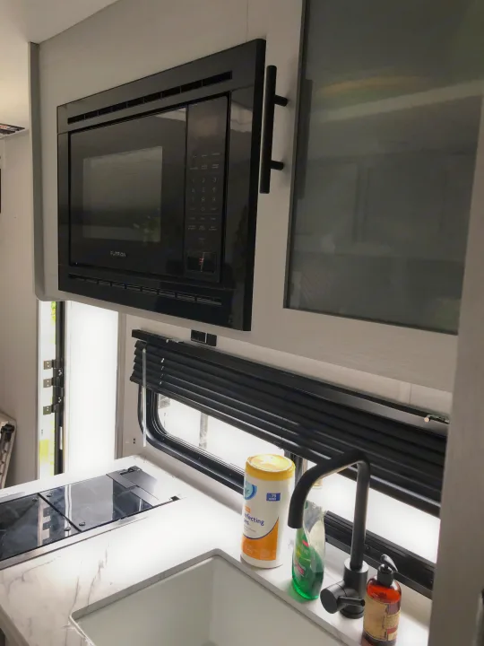 A sleek, modern kitchen in an RV rental, showcasing an overhead microwave, induction stovetop, sink, and cleaning supplies.. Forest River Wildwood 2021