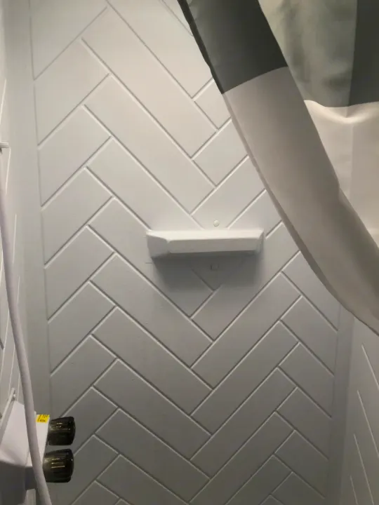 Inside an RV rental: a modern shower with white herringbone walls, a built-in shelf, and a striped curtain.. Forest River Wildwood 2021