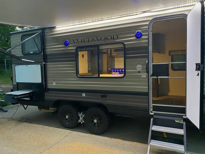 An RV rental: a Forest River Wildwood travel trailer with an extended LED-lit awning, open door, and outdoor kitchen.. Forest River Wildwood X-Lite 2019