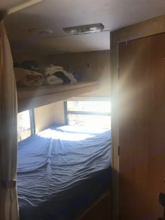 Cozy RV rental interior featuring comfortable bunk beds with a blue sheet and bright windows, ideal for travel.. Keystone Hideout 2009