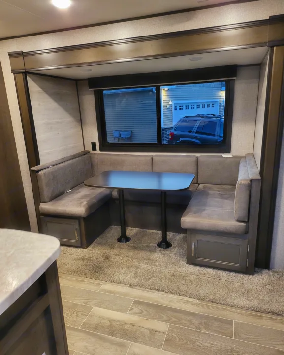 RV rental interior showing a dinette setup with grey upholstered benches, a central table, and a large window.. Jayco Jay Flight SLX 2021