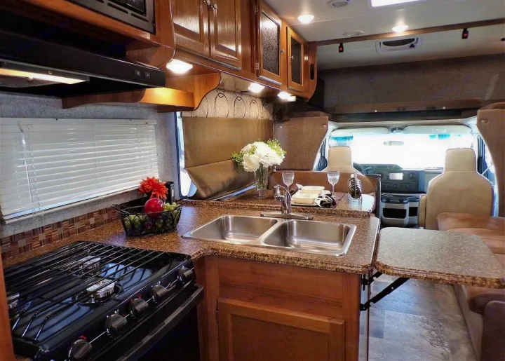 Inside this RV rental: a modern kitchen with stove, double sink, and ample counter space, leading to dining and cockpit.. Forest River Coachmen Leprechaun 2018