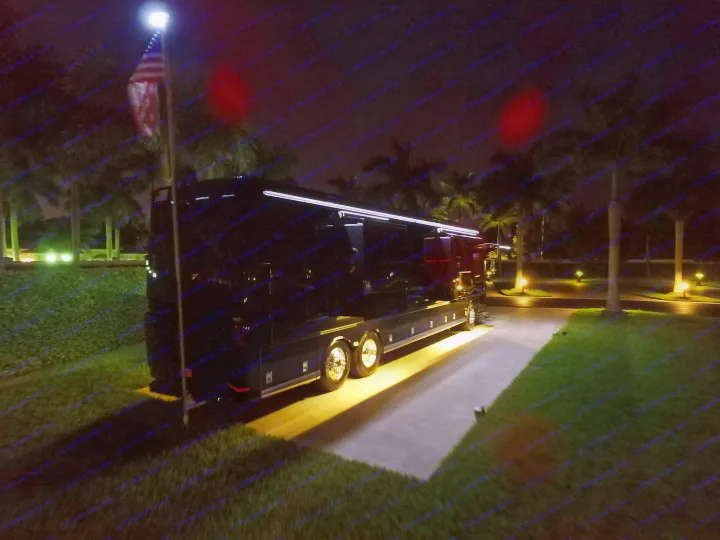 Night scene: a luxurious black RV rental parked on a lit driveway with palm trees and an American flag.. Other Other 2017