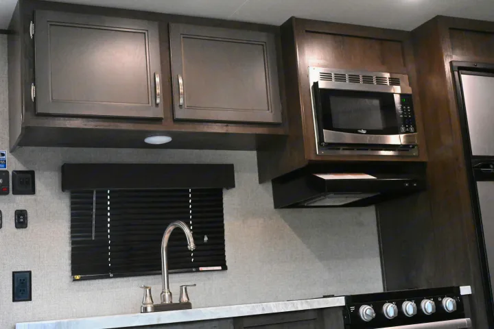 Modern **rv rental** kitchen featuring dark cabinets, microwave, stove, and sink. Ideal for travel cooking needs.. Jayco Jay Flight SLX 2021