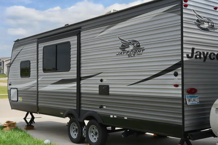 A gray Jayco travel trailer, ready as an RV rental, parked with stabilizing jacks. Features visible include windows, an awning, and hookups.. Jayco Jay Flight SLX 2021