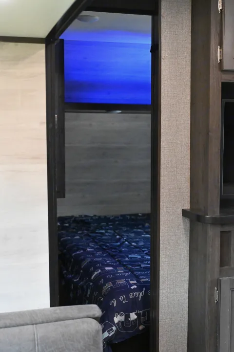 Inside a cozy RV rental bedroom, featuring blue ambient lighting and a fun camper-themed comforter, highlighting a compact interior.. Jayco Jay Flight SLX 2021
