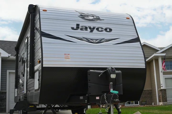 Front view of a Jayco travel trailer, ideal for an RV rental. Notice its light gray corrugated siding, black diamond plate, and hitch.. Jayco Jay Flight SLX 2021