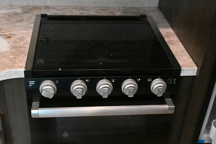 An RV rental's black gas stove and oven unit, with control knobs and a glass cover for cooking.. Jayco Jay Flight SLX 2021