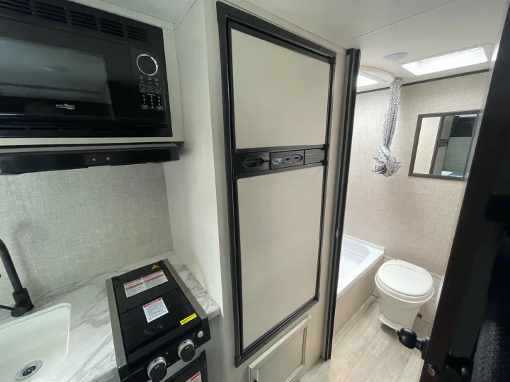 Modern **rv rental** interior: a compact kitchen with microwave, stove, and sink, next to a large fridge and a full bathroom.. Jayco Jay Flight SLX 7 184BS 2022
