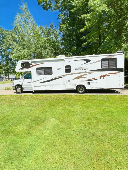 A white Sunseeker Class C RV, ideal for an rv rental, is parked on a driveway with green grass and trees in the background.. Forest River Sunseeker 2013