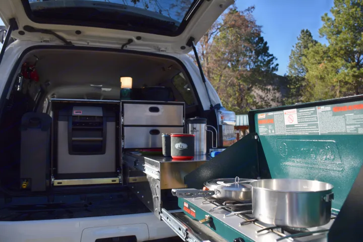 RV rental car camping setup with a slide-out kitchen, fridge, and portable stove, perfect for overlanding adventures.. Toyota 4Runner 2021