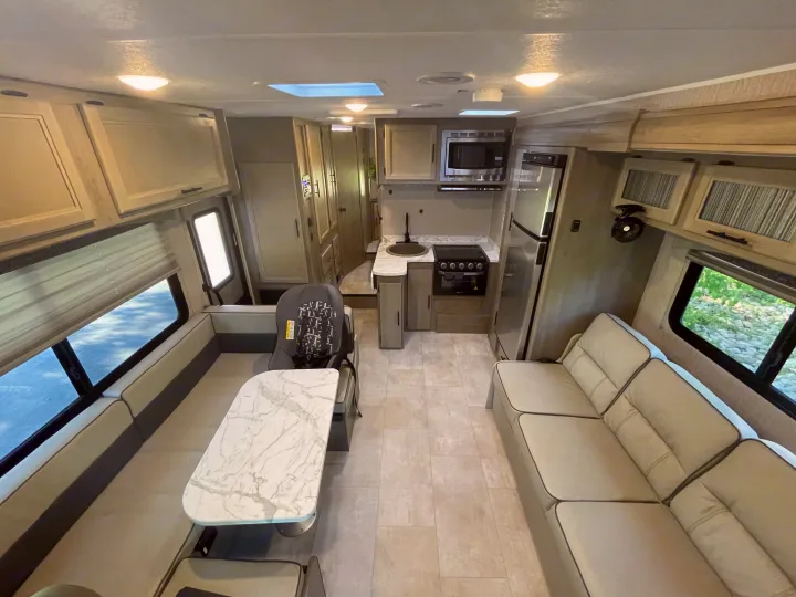 Modern RV rental interior: kitchen, dinette with car seat, and sofa. Bright, clean living space for travel.. Other Other 2022