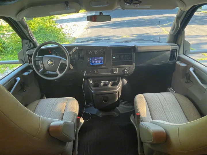 The spacious interior of a modern RV rental van, showing its dashboard, steering wheel, and front grey seats.. Other Other 2022