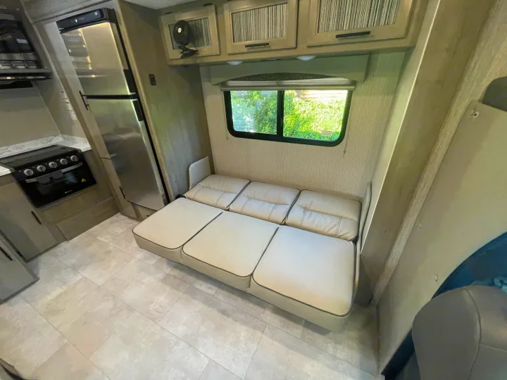 Cozy RV rental interior featuring a full kitchen with stove and fridge, a convertible sofa bed, cabinets, and a window.. Other Other 2022