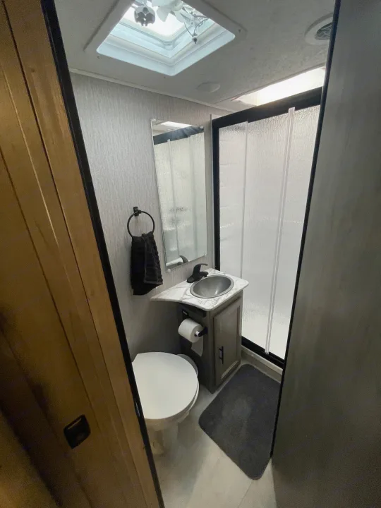 A view inside a clean RV rental bathroom, showing a toilet, vanity with sink, mirror, and a glass-enclosed shower.. Other Other 2022