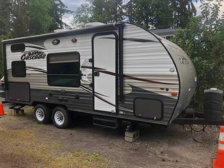 Grey and white Cascade Limited travel trailer, an ideal RV rental, parked on gravel with its door open.. Forest River Cherokee 2015