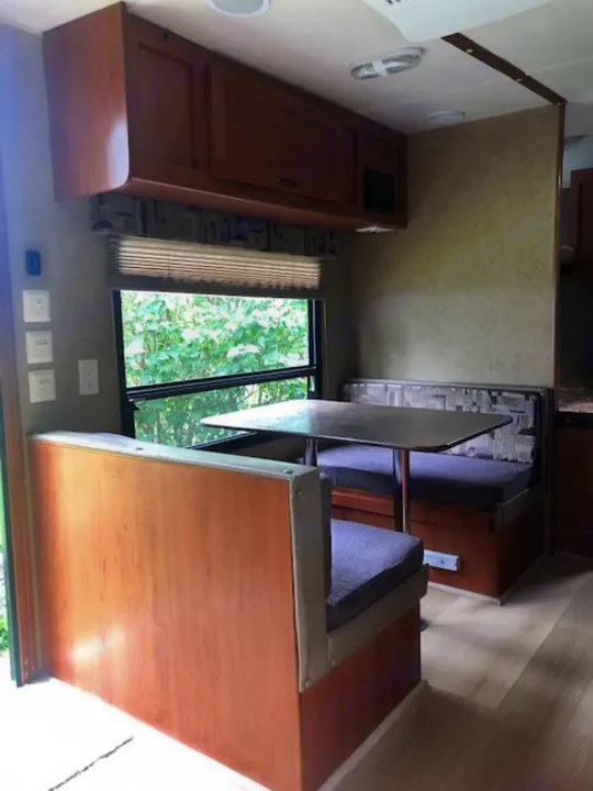 RV rental interior: dinette with table and benches, wood cabinetry, and a large window offering an outdoor view.. Forest River Cherokee 2015