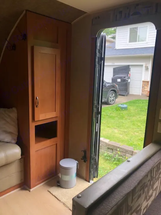 Inside an RV rental, looking out the open door. Features include a portable toilet, built-in storage, and seating.. Forest River Cherokee 2015