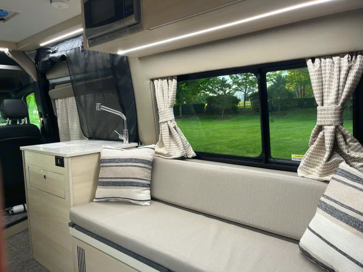Modern rv rental interior: kitchenette, cushioned seating, and window view of green landscape.. Tiffin Motorhomes Cahaba 2021