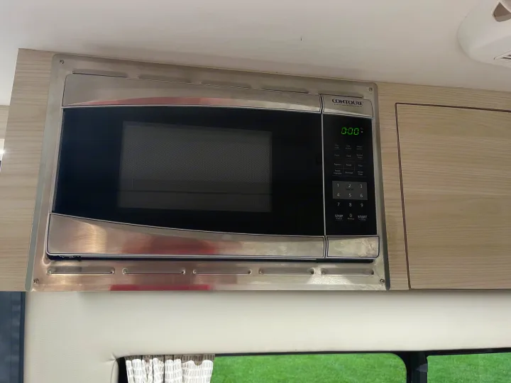 This RV rental kitchen features a built-in stainless steel microwave oven, displaying '0:00' on its digital clock.. Tiffin Motorhomes Cahaba 2021