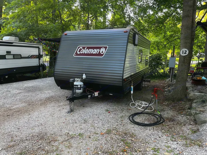 This gray Coleman rv rental is set up at a shaded campground site, complete with water and propane hookups.. Coleman CM17B21 2021