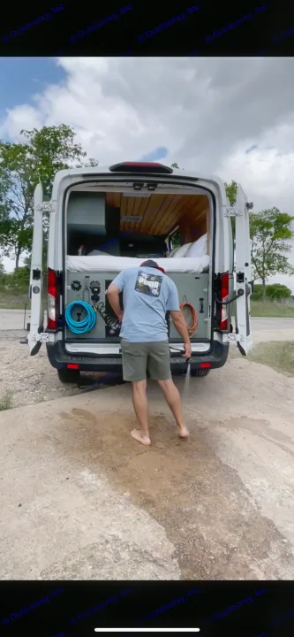 Barefoot man rinses off at the back of an RV rental. This custom camper van offers convenient outdoor water access.. Ford Transit 2019