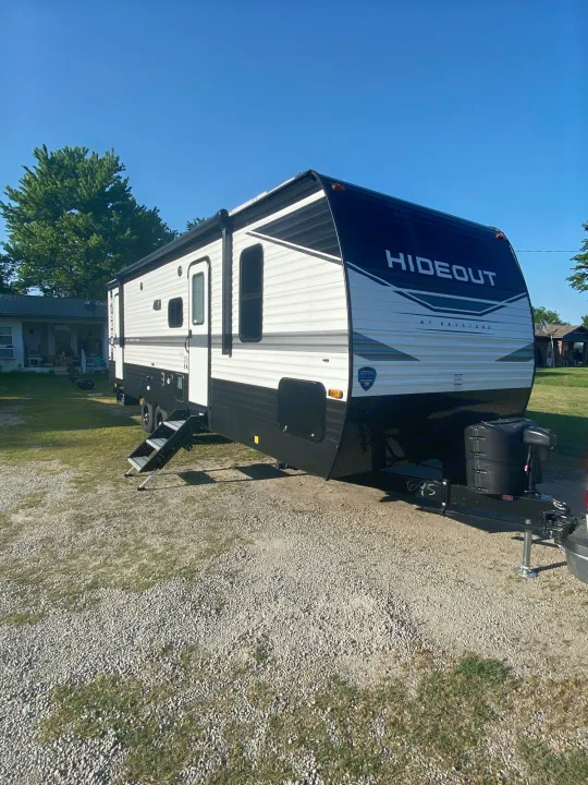 New Keystone Hideout RV rental, a white and black travel trailer parked on gravel with extended steps.. Keystone Hideout 2022