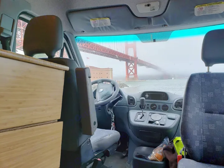 Experience a scenic RV rental view of the Golden Gate Bridge through the fog from inside a converted van, featuring a wooden cabinet.. Mercedes Sprinter 2006