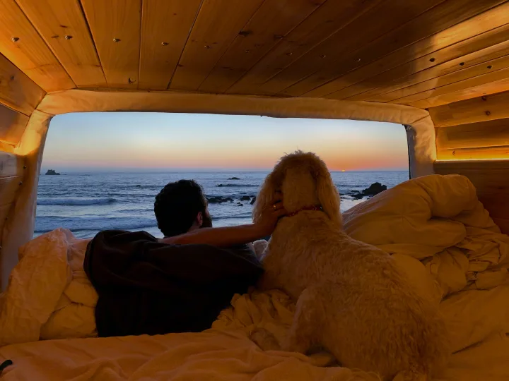 Man and dog watch a beautiful ocean sunset from their cozy RV rental bed.. Mercedes Sprinter 2006