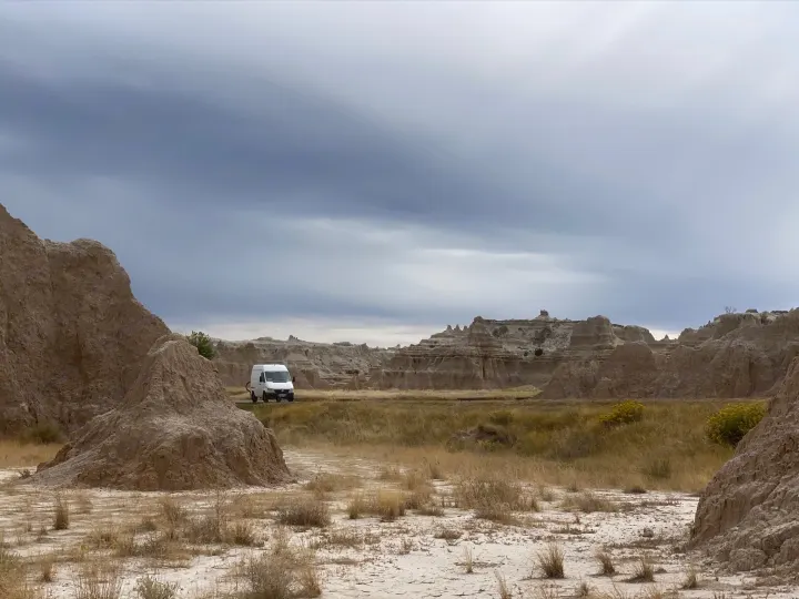 An rv rental van on a road through dramatic Badlands rock formations under cloudy skies.. Mercedes Sprinter 2006