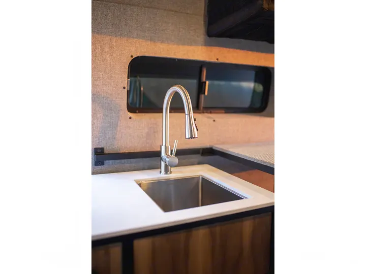 Enjoy a functional RV rental kitchen: sleek stainless steel sink, modern faucet, white countertop, and fabric walls.. Ford Transit 2021